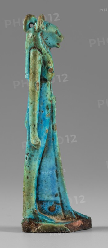 Amulet - figurine of a lion-headed goddess. A lion-headed goddess, in a tripartite wig and a narrow robe, walks with a lotus scepter in her left hand the right one is lowered. Presumably the goddess Sekhmet. Materials/type: amulet. Subject: lion-headed goddess, lionesses; Egyptian deities Sekhmet, Wadjit, Bastet suggested. Function: grave goods. Date: 664–332 BC, Late Period, Egypt. Dimensions: height 8.8 cm, width 1.7 cm. Maker: unknown., A slender standing figurine with a stylized animal head and elongated body rendered in a mix of bright turquoise, aqua, pale green, and spots of darker blue, with scattered patches of brown and rust-colored discoloration; the figure has an upright posture, long arms held close to the torso, a defined chest and hips, a long skirt-like lower garment, a rounded base with worn edges showing dark brown and reddish tones, and a small loop or hole near the back of the head.
