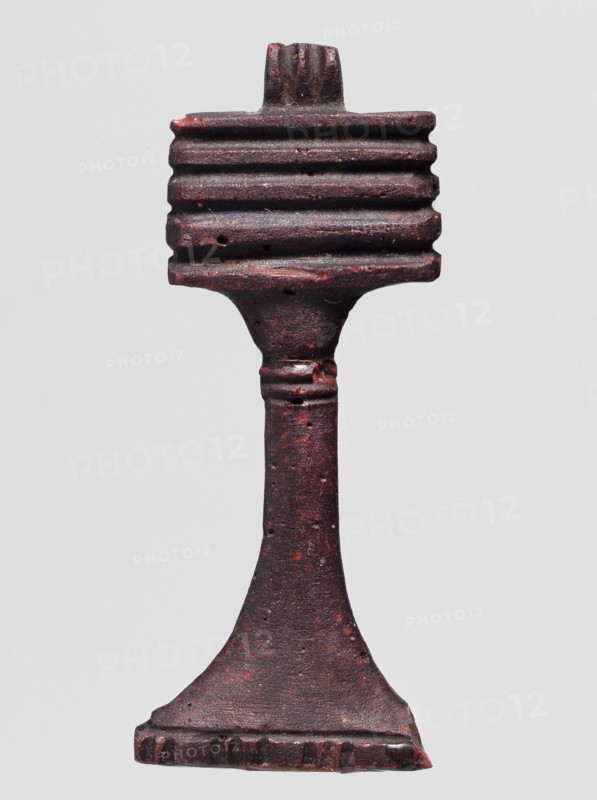 Amulet - djed pillar, A brown glass amulet in the shape of a djed pillar with five crossbars and a tall, slender leg that widens significantly at the bottom. Djed pillars iconography; protective amulet; grave goods; hieroglyphs. Ptolemaic Period, 332–30 BC, Egypt. Amulet; height 5.6 cm, width 2.1 cm., A single vertical object with a textured surface, appearing to be made of a dark reddish-brown material with areas of deeper red and small flecks of lighter color, set against a plain light gray background; the object has a rectangular top section with a series of horizontal ridges, a narrower midsection that tapers and shows a few raised rings, and a flared base that widens into a flat foot with a notched edge.