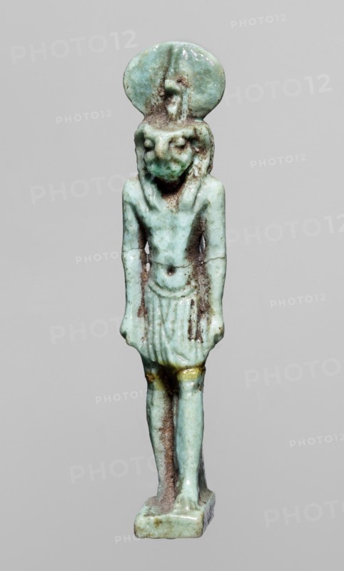 Amulet — god Re-Harakhte; maker, Re-Harakhte mythology; Egyptian deities; solar disk and uraeus iconography; Egyptian religion; Late Period, 664–332 BC, Egypt; material: amulet; dimensions: height 4.2 cm, width 0.8 cm, depth 1.3 cm., A small statuette of a standing figure in a bluish-green material with areas of brown discoloration, wearing a short skirt and a rounded headpiece, with an elongated torso and straight arms hanging at the sides, a rounded base supporting the feet, and small touches of yellowish color near the upper thighs.