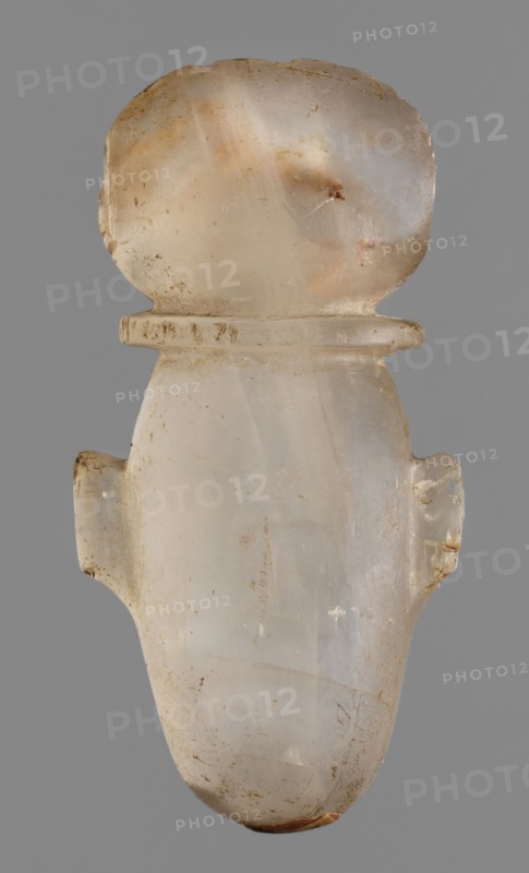 Amulet - heart with a sun disc;, sun disc iconography; grave goods; protective amulet; Late Period, Egypt, 664–332 BC; amulet; height 5 cm, width 2.5 cm, depth 1.5 cm, A translucent, rounded object with a bulbous top and a tapered lower body is shown against a solid gray background, appearing to be made of a milky, off-white material with areas of pale beige and faint amber tones, and small patches of brown discoloration. The surface shows a few rough spots and minor chips, with subtle striations and cloudy internal variations in color. There are small protrusions on each side near the middle, and a thin flange-like ridge below the bulbous top. Overall the colors visible are off-white, beige, pale amber, brown, and gray.