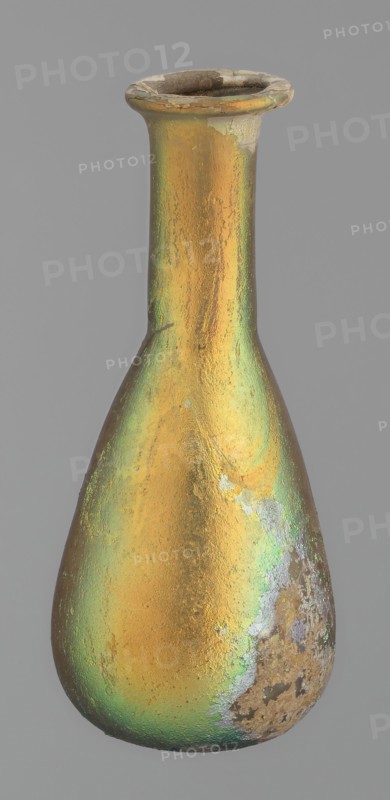 Flask, unknown eastern workshop, glass, antiquity, Roman Empire. Flask with a slender, pear-shaped body and a lower neck ending in a ring-shaped rim. Flat bottom. Covered with multicolored patina. 1st–2nd century, unknown place of origin; vessel, height 9.4 cm., A tall, narrow-necked vessel with a flared rim and a bulbous body, showing a textured iridescent surface with dominant gold and green tones and areas of brown and gray patina; the rim and parts of the neck have worn and chipped edges revealing a duller, rougher material, and there are patches of mottled discoloration and surface pitting near the base and on one side.