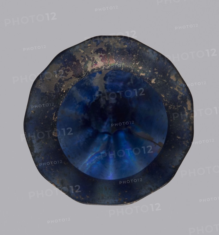 Krateriskos, unknown eastern workshop, Goluchów Greater Poland Voivodeship — 3rd–4th century AD, vessel, height 3.4 cm, width 3 cm, A circular object with an irregular rim is centered against a light gray background; the object shows a deep blue central area with iridescent shifts of lighter blue and purple, surrounded by a darker, mottled ring that includes shades of dark blue, black, brown, and hints of green and gold.