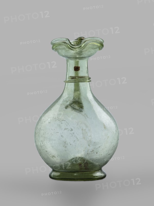 Oinochoe, Transparent, light green glass; spherical belly on a foot with a clearance, created by pressing inward the central part of the bottom of the vessel; decoration on the cylindrical neck in the form of a single glass thread of the same color, wound horizontally. The handle is glued to the arms and extends in an arc to the edge of the trefoil rim; free-blown. 4th century, Cyprus; vessel, oinochoe; base diameter 4.8 cm; weight 0.062 kg., A translucent glass vessel with a round body and a narrow neck topped by a flared, undulating rim, showing a pale green tint overall with subtle variations of lighter and darker green, a few areas with faint cloudy whitish streaks and some darker green spots, a group of small bubbles and imperfections visible within the glass, and a smooth green base.