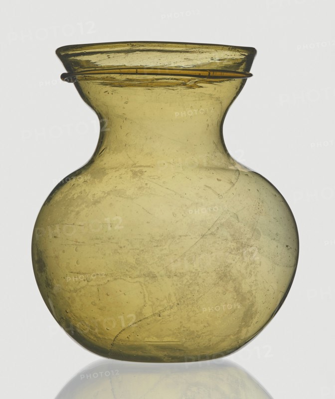 A viceless vessel, Goluchów Greater Poland Voivodeship, below the edge a glass thread is applied horizontally, unspecified place of origin, vessel, height 12.4 cm, width 10.7 cm, A translucent yellow-green glass vessel with a rounded body that narrows into a short neck and flares outward at the rim, showing a few surface imperfections and internal bubbles; a thin glass ring encircles the rim; the vessel sits on a reflective surface, and the background is a light neutral color.
