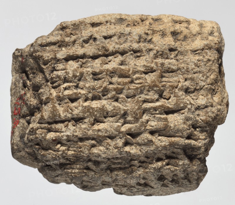 Cuneiform tablet with receipt, unknown Babylonian official role classification of creator, cuneiform tablets, Neo-Babylonian document, trade, Rectangular tablet, slightly convex, horizontally oriented. Three corners broken off; cracks on the lower and left sides; 9 lines of cuneiform text on the obverse, 2 on the lower side, 9 on the reverse. 6th century BC; Neo-Babylonian period, Babylonia Iraq, Southern Mesopotamia, administrative document, height 3.8 cm, width 4.5 cm, thickness 2 cm, A rough, irregularly shaped stone with a textured, pitted surface fills the frame, showing layered, incised grooves and ridges across its face; the stone is primarily beige and light brown with areas of darker brown and small flecks of off-white, and there is a small area of red on one side.