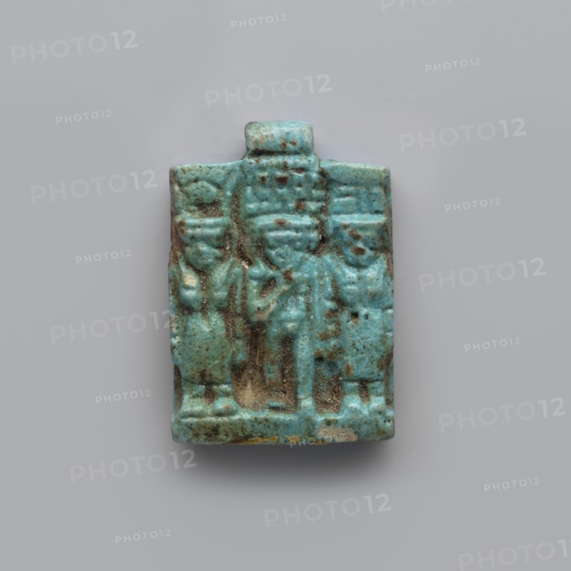Amulet – plaque with a triad of deities, Harpocrates Horus, Isis, Nephthys. Amulet in the shape of a plaque with a triad of deities standing on a base: center figurine of Horus, left Isis, right Nephthys. Back of the plaque is flat; pendant above the upper edge. Date: 664–30 BC, Late Period–Ptolemaic Period probable. Find country: Egypt. Object type: amulet. Dimensions: height 3.3 cm; width 2.2 cm; depth 0.7 cm., A small rectangular object with a raised relief depicting a group of three standing figures, rendered in a turquoise blue with areas of darker brownish-green patina and small pale beige spots, showing worn and pitted surfaces and textured details in the figures' clothing and headpieces, set against a smooth light gray background.