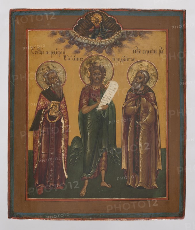 Icon: Saints John the Baptist, Porphyry, and Sergius of Radonezh before Christ, Northern School 1500–1917. In the center St. John the Baptist, dressed in an animal skin and a cloak, holds an unrolled scroll. On the left is St. Porphyry in bishop's robes; on the right St. Sergius of Radonezh in monk's robes. Above, on the axis, Christ Pantocrator is shown knee-deep in clouds, blessing with both hands. The icon is meticulously rendered with attention to detail; colors are contrasting—predominantly cinnabar, ochre, and green. Identifying inscriptions appear in the background of the central part. 19th century, Russia. Dimensions: height 31.0 cm; width 26.2 cm., A painted panel showing a religious scene with three standing haloed figures against a golden background, framed by a brown border with blue and red inner edges; the central figure is barefoot, wearing green and red draped robes and holding a pale scroll, flanked by two bearded figures in ornate robes and cloaks—one on the left wear...