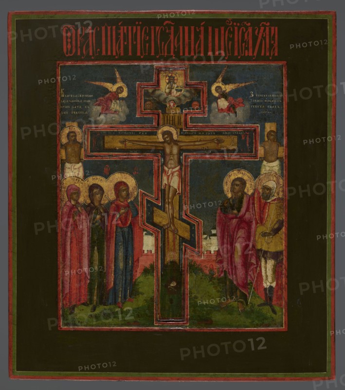 Icon: Crucifixion of Christ on Golgotha, Old Believers workshop. In the center a recessed eight-pointed wooden cross depicts Christ stretched out. Above are God the Father and the dove of the Holy Spirit. To the left of the cross: Mary, the mother of Christ, and two women; to the right: St. John and the centurion Longinus. Behind them are the two thieves on crosses. In the upper part angels in the clouds turn toward the Crucified One, with cloth covering their hands. Background shows the symbolic walls of Jerusalem and a view of the city. Colors are rich, contrasting, and realistic; a striking dark blue sky. Inscriptions in white paint are visible in the upper corners; an identifying inscription in vermilion is placed in the upper field. 18th century, Wietka workshop; icon; height 49.5 cm, width 44.3 cm., A painted panel showing a central crucifix with a body on the cross, outlined by a bold border, set against a dark blue background within a rectangular frame; on the left side of the ...