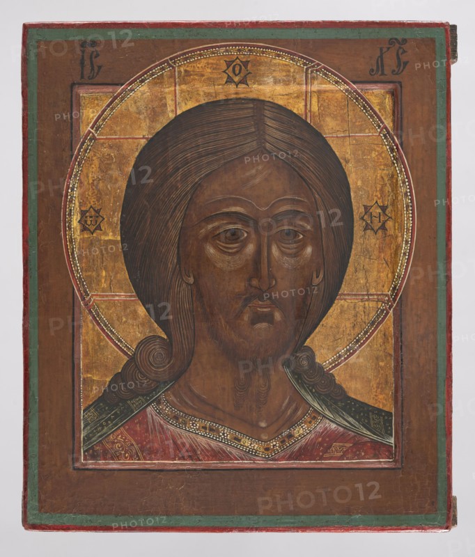 Icon: Christ the Savior. Old Believer Popovtsy workshop, Russian workshop. Subject: Jesus Christ. Medium/type: icon. Description: The face of Christ is depicted in the kovcheg with a brown complexion brightened by white tones on the forehead, eyelids, under the eyes, chin, and around the mouth. Eyes large; nose long and straight; hair parted in the middle, falling in circular locks on the shoulders; beard small and bipartite. Christ wears a red chiton with a gold border decorated with a delicate plant ornament, and a malachite himation with an ornament. Around the head is a cruciform halo; the letters on the arms of the cross are placed in double overlapping rhombuses—gold and red. The background of the kovcheg is gilded. Style linear, with tendencies toward decorativeness and stylization. Date: 2nd half of the 19th century. Place: Western Russia . Dimensions: height 31 cm, width 25.5 cm. Inscriptions: present. Iconography: star, halo., A painted panel showing a frontal portrait of a p...
