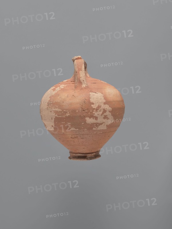 Jug, unknown Aswan workshop. Jug with a rounded rim, a narrow and upwardly flaring neck with a ring-shaped flange. Spherical body with a large ribbon-shaped handle attached to the lower part of the body and the middle part of the neck. Ring-shaped foot. Traces of turning slightly smoothed. Exterior covered with red-brown engobe, interior beige-pink, even. Kaolin ceramic mass Gempeler type IA. Egyptian sigillata / Egyptian pottery; Coptic vessels, tableware. 5th–6th century. Findspot: Edfu. Vessel jug. Height 14.1 cm; lip diameter 2.4 cm; neck diameter 1.8 cm; body diameter 11.4 cm; base diameter 4.6 cm., A single rounded ceramic vessel with a narrow neck and small flared foot is centered against a plain gray background; the vessel shows a weathered surface with patches of lighter worn areas and a base color of terracotta orange, with visible rough texture and small chips, and a few darker brownish spots and streaks.