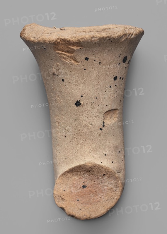Fragment of a transport amphora body stamped with a Rose of Rhodes, unknown Rhodian workshop; stamp impressions; trade. Fragment of a transport amphora stamped with a Rose of Rhodes and the inscription Chresimou, ca. 280–ca. 220 BC, Rhodes; vessel stamped body, height 6.8 cm, width 10 cm, A roughly cylindrical, tapered object with a flared rim and a rounded base displayed against a neutral gray background; the surface is a sandy beige with scattered small black speckles and a few darker spots, and there are areas of slightly darker brownish-beige where the texture appears rougher or chipped, including a small indentation on one side and a worn, uneven rim.