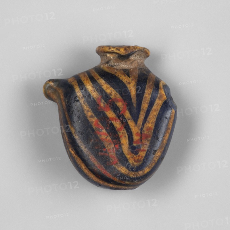 Pendant in the shape of a flattened oval vessel resembling the ib amulet. Low, narrow neck with a rounded edge. Two handles in the form of cylindrical bulges on the sides in the upper part. Zigzag decoration made by embedding glass thread. 1st century BC–1st century AD, Egypt. Amulet; height 1.6 cm., A small rounded object with an irregular top opening and a short spout-like projection, shown against a light gray background; the object has a dark base color with bold curving stripes in yellow ochre and accents of muted red, and its surface appears slightly worn with some rough and pitted areas.