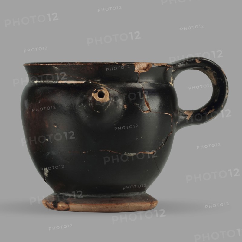 Askos with spout and strainer, unknown Attic workshop, Greek pottery toilet vessel with tubular spout and ribbon handle; top covered with a strainer. 5th century BC, Attica; vessel askos. Height 6.2 cm, width 8.3 cm, depth 9 cm, weight 0.09 kg., A rounded ceramic vessel with a single loop handle and a small protruding spout, shown against a flat gray background; the vessel has a glossy black surface with areas of worn brownish-orange clay visible where the black coating has chipped, and several hairline cracks and missing flakes revealing the brownish-orange beneath; the base shows exposed brownish-orange clay with darkened spots, and the handle interior has worn lighter areas; overall colors visible include black, brownish-orange, and gray.
