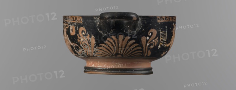 Red-figure bowl with Eros and a young woman, /workshop, red-figure pottery, bowl kylix, yellow clay tending to red, glossy black engobe, some elements painted white. Bowl with a ring-shaped base with two vices attached to the rim horizontally; palmettes beneath the vices. Belly decorated with two scenes: Scene A — young woman semi-reclining on the ground, facing left, holding a wreath in her left hand and a woven basket on her outstretched right hand; dressed in a long smooth chiton; wearing a pearl necklace and double bracelets on the wrists; hair tied in a bun with a kekryphalos. Scene B — Eros flying, facing left; in the right hand a musical instrument and in the left a wreath with a ribbon; hairstyle and jewelry match Scene A bun with kekryphalos, double bracelets, pearl necklace; additionally ankles adorned with bracelets and head with a diadem; entire figure shows hermaphrodite features. Condition: numerous chips, engobe dull in places. 3rd quarter of the 4th century BC, Apulia o...