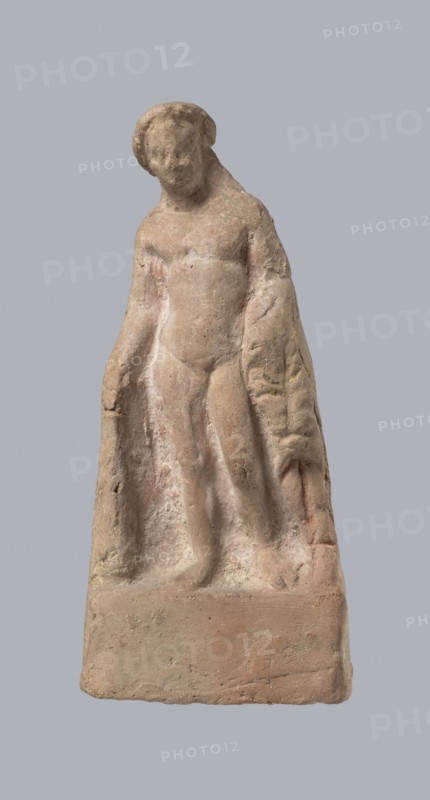 Terracotta figurine of Heracles. Figurine of a standing naked Heracles in a contrapposto pose; cloak thrown over his back. His right hand rests on a rock, and in his left he probably holds a club. Terracotta, made from a mold. Figurines of nude men; Heracles Greek mythology. Condition of preservation: good. 2nd–1st century BC. Asia Minor. Height 14.3 cm., A weathered stone sculpture of a standing human figure on a rectangular base, showing a simplified torso, limbs, and head with softened facial features, drapery or cloak hanging behind and to the sides, and a rough, pitted surface texture; visible colors include beige, light brown, pale pink, and hints of gray.