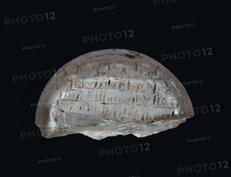 Fragment of an amulet with an Arabic inscription, message provenance, Islamic art, Arabic culture, amulets, inscriptions, Arabic language, inscription probably with magical meaning, 11th–12th century, Egypt, amulet, height 1.1 cm, width 2.5 cm, depth 0.9 cm, A translucent, dome-shaped object with a smooth curved top and an irregular jagged bottom edge sits against a dark black background, showing a clear to milky white appearance with areas of pale brownish and grayish inclusions and surface marks, and a small patch of muted red near one edge; the surface bears shallow linear grooves and scratches arranged in horizontal groupings and vertical strokes, and light reflects off glossy and slightly frosted areas creating subtle highlights and shadows.