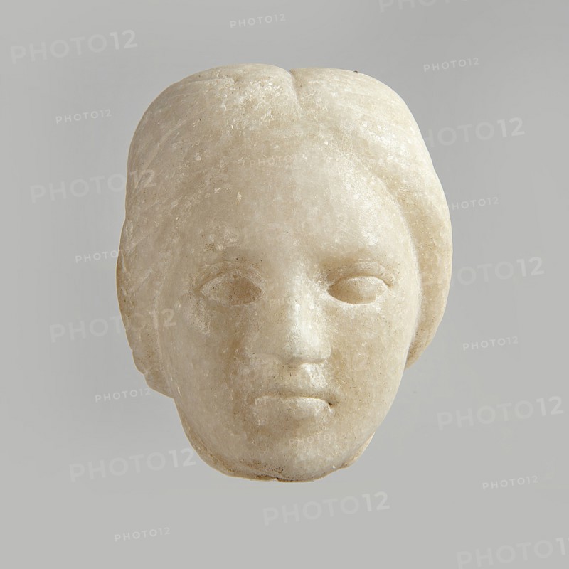 Fragment of a female figurine. Fragment of a small-sized sculpture or sculptural group. The depiction has portrait features. The face is oval, the nose is large, the mouth is closed in a slight grimace. 2nd–3rd century AD, Egypt. Terracotta figurine, sculpture; height 8.5 cm, width 4.5 cm, depth 5.5 cm., A pale stone sculpted head with smooth rounded contours and a neutral expression is centered against a light gray background; the surface shows subtle variations of off-white, cream, and beige with faint textured speckles, shallow eye sockets and simplified facial features, a defined nose and lips, and hair indicated by gentle grooves framing the sides and top.