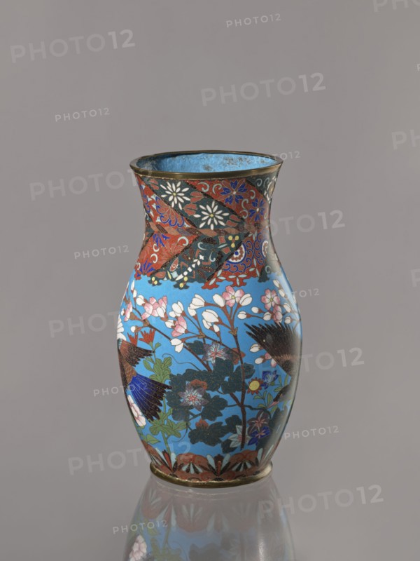 Vase, Revindication Kraków. Doves, flowers iconography; Japanese art; Japanese culture. Choynowski, Józef 1833–ca.1915. Birds. Meiji 1868–1912. Peonies, chrysanthemums, wolfberries, kachôga iconography, sakura iconography. Cloisonné enamel. Belly flowing smoothly into a short, thick, slightly parted neck. Cloisonné enamel on copper; brass foot and spout frame. Ca. 1870–1880 Meiji Period, 1868–1912. Japan, Nagoya. Vessel. Height 26.5 cm; width 12.6 cm., A decorative vase with a flared rim and rounded body sits against a plain gray background, featuring a glossy sky-blue base color covered with floral and bird motifs in a palette of red, white, pink, green, dark blue, black, and gold; the neck area shows a band of red and black patterned sections with white and blue floral accents, while the main body displays branches with white and pink blossoms, dark green leaves, and stylized birds with dark blue and black feathers, and a narrow gold rim and base.