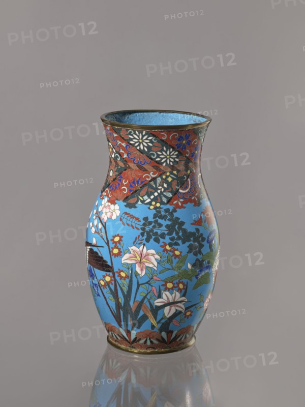 Vase, doves, flowers iconography, Japanese art, Japanese culture, Choynowski, Józef 1833-ca 1915, birds, Meiji 1868-1912, peonies, chrysanthemums, wolfberries, kachôga iconography, sakura iconography, cloisonné enamel. Belly flowing smoothly into a short, thick, slightly parted neck. Cloisonné enamel on copper; brass foot and spout frame, ca. 1870–1880 Meiji Period, 1868–1912, Nagoya, Japan. Vessel; height 26.5 cm, width 12.6 cm., A single decorative vase with a flared rim sits against a plain gray background, the vase showing a bright sky-blue main field with a band of darker patterned decoration near the top; the surface is covered with floral and foliage motifs including lilies and other blossoms in colors such as pink, white, red, yellow, green, and blue, with black and dark green leaves and stems. The upper patterned band contains swirling designs in red, black, blue, white, and gold tones, and the rim and base edges are accented with a metallic bronze color. The vase rests on a r...