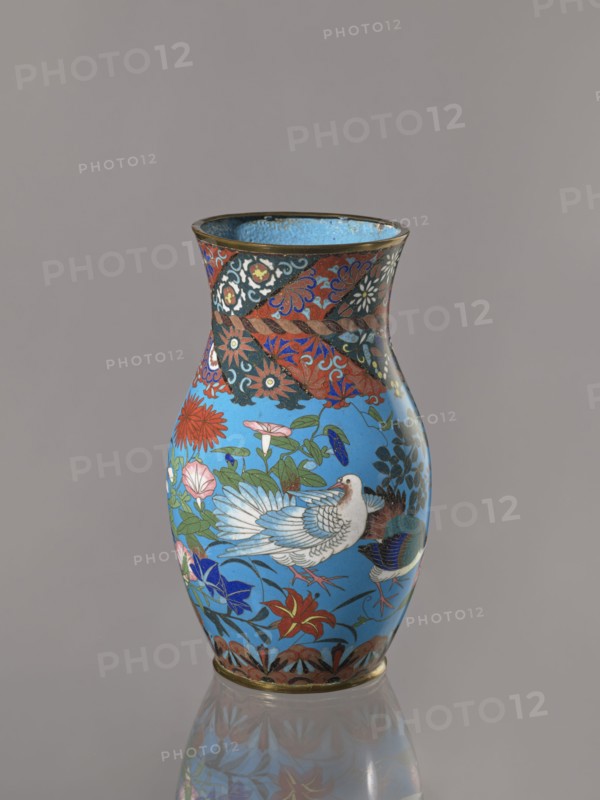 Vase, Vase with a thick neck, parted towards the spout. Cloisonné enamel on copper; the spout and foot are enclosed by brass rings. Decorated with doves, flowers lilies, chrysanthemums, sakura, wolfberries, butterflies, dragonflies, kachôga-style bird-and-flower imagery. Japanese, Meiji period, ca. 1870–1880; Nagoya. Vessel. Height 26.5 cm; width 15.5 cm., A rounded vase with a flared rim stands against a plain neutral background, its surface dominated by a bright turquoise-blue field decorated with a stylized white bird with detailed feathering, surrounded by a profusion of floral motifs and leafy vines in red, pink, green, dark blue, and black; the neck and shoulder feature a contrasting band of ornate patterns in red, black, and gold tones with swirling floral and geometric elements, and the base is edged with a narrow metallic rim and a patterned border in brown and gold; the glossy finish produces a subtle reflection of the vase on the surface beneath it.