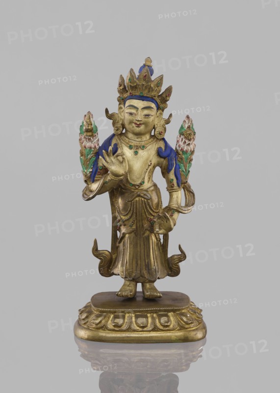 Maitreya Buddha of the Future, Tibetan Buddhist art, figurine, bodhisattva iconographic, lotus throne iconographic, Buddhist art, Buddha of the Future, 19th century, Southern China, Tibet, sculpture, height 16.8 cm, width 7.6 cm, A gilded statue of a standing figure on a carved pedestal, with a crown and ornate headdress, a serene facial expression, and stylized hair; the figure wears draped garments with decorative folds and layered jewelry, and has one hand raised in a gesture while the other holds an object; there are a few ornamental floral or flame-like elements near the shoulders, and small adornments on the body and skirt; visible colors include gold, blue, green, and pink, set against a plain light gray background.