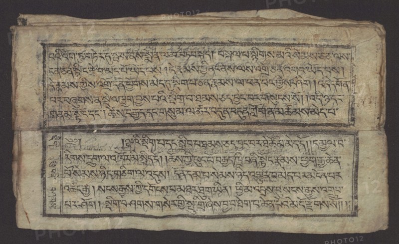 Buddhist text - Formula of Repentance Tib. sdig bshags gser gyi spu gri bzhugs so, author unknown. Book in the Tibetan pecha style; xylographic print in the disciple script dbu can. 16 folios folio numbering 2–15 recto, first verso. Print on thin handmade paper, clear translucency. 19th century, Tibet. Graphic prints; Buddhist art; Tibetan. Dimensions: width 25.5 cm, height 7.8 cm., A rectangular sheet with worn, textured paper rests against a dark background; the paper is off-white to beige with areas of light brown discoloration and darker stains, and it appears creased and slightly frayed at the edges. Two bordered horizontal panels occupy the sheet, each containing dense, flowing handwritten strokes in dark ink that form repeating linear patterns across the panels; the ink ranges from deep black to faded gray in places. Narrow black borders frame each panel, with a thicker horizontal band separating them that shows smudging and uneven ink. The left edge of the sheet shows a folded ...