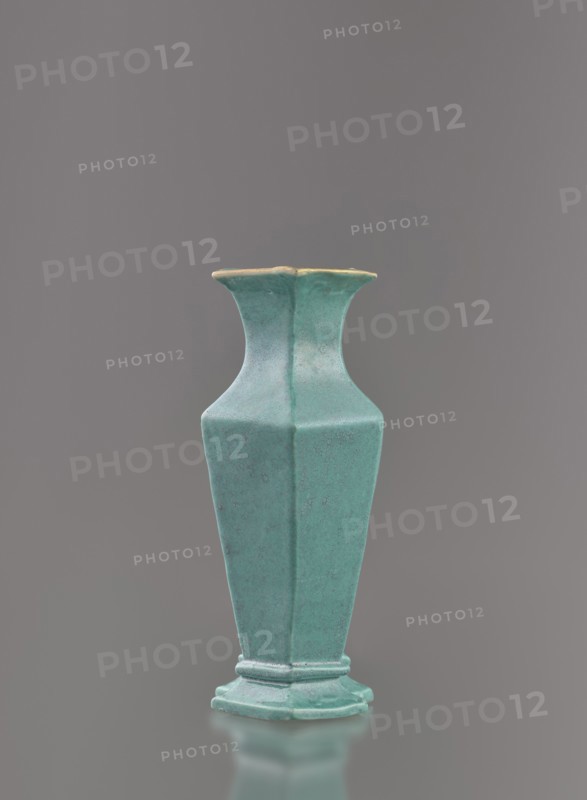 Vase, Chinese, Qing dynasty 1644–1911, 19th century. Ceramic vessel covered with a turquoise glaze with manganese spots. Height 11.6 cm; width 4.9 cm; depth 7.1 cm; weight 0.15 kg., A single tall vase with a flared rim and a hexagonal body stands centered against a neutral gray background; the vase is a muted turquoise color with subtle darker speckling and a slightly lighter rim edge, and it rests on a stepped hexagonal base that shares the same turquoise hue.