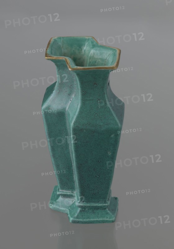 Vase, 19th century, China; Qing dynasty; Chinese ceramics. Covered with a turquoise glaze with manganese spots. Vessel with cover; height 11.6 cm, width 4.9 cm, depth 7.1 cm, weight 0.15 kg., A green ceramic vase with a textured, crackled surface and a slightly glossy finish sits against a neutral gray background; the vase has an angular, faceted form with a flared top rim that shows a thin band of yellowish-gold along its edge, an irregular square-like mouth with inward curves, a tapered body with defined vertical facets, and a stepped base, with visible variations in green tones ranging from lighter to darker areas and subtle worn spots.