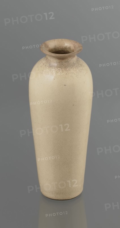 Cylindrical porcelain vase tapering toward the bottom with flat rim; light cream glaze with fine cracklework. Wooden round flat saucer on three legs. 19th century, Japan; Japanese, Edo 1603–1868; ceramics; saucers; vases; cracklework decoration. Vessel height 21.1 cm, diameter 8.4 cm, weight 0.6 kg., A tall, narrow ceramic vase with a rounded shoulder and flared rim sits against a smooth background; the vase surface is a creamy beige with a network of fine crackle patterns concentrated near the rim and subtly visible across the body, and the rim area shows a slightly darker, brownish-beige tint.