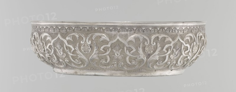 Bowl, Islamic art, Turkish culture, Ottoman dynasty 1299–1922, geometric motifs, plant ornament, tugra of Abdulhamid II Ottoman sultan; 1842–1918, 1876–1909, Turkey, silver hammam bowl, vessel, height 5.6 cm, diameter 19.0 cm, A shallow ornate bowl with raised scrolling floral and foliate motifs around its exterior, featuring curving leaf shapes and stylized blossoms in relief, a decorative patterned band near the rim, and a smooth flat base; the visible colors are silver, light gray, and pale metallic tones.