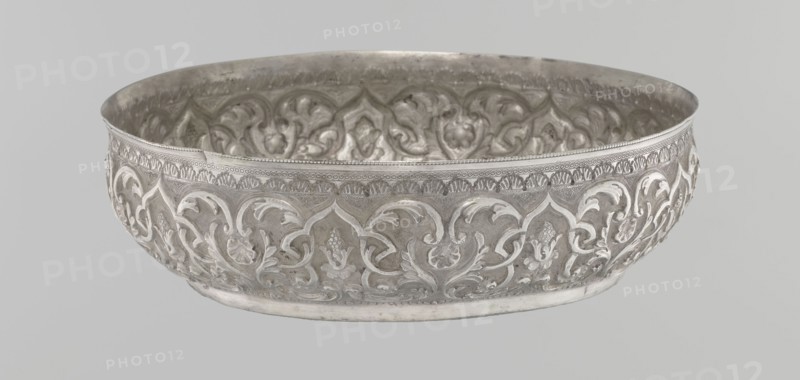 Bowl, purchased; Islamic art, Turkish, Ottoman dynasty 1299–1922; geometric motifs and plant ornament; tughra of Abdulhamid II Ottoman sultan; 1842–1918; dated 1876–1909; silver hammam bowl; Turkey; vessel; height 5.6 cm, diameter 19.0 cm, A shallow round metal bowl with ornate raised floral and scrolling patterns covering its exterior and interior, rendered in metallic silver tones with areas of darker gray patina and lighter reflective highlights; the rim has a band of small repeating decorative elements, and the interior shows similar embossed motifs creating a textured surface; the background is a uniform pale gray.