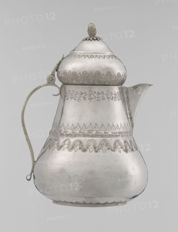 Teapot, 19th century, Turkish Ottoman dynasty, 1299–1922. Silver vessel teapot, height 17.0 cm, diameter 10.9 cm, weight 320 g. Decoration: geometric motifs, plant ornament lambrequin, zigzag. Function: teapot/jug. Culture: Islamic art., A metallic pitcher with a rounded, bulbous lower body tapering to a narrower midsection and topped by a domed lid with a small finial, shown against a plain light background; the pitcher displays decorative etched patterns around the neck, midsection, and near the base, with a curved spout on one side and a slender handle attached on the opposite side; visible colors include silver tones of the metal and subtle variations of gray.