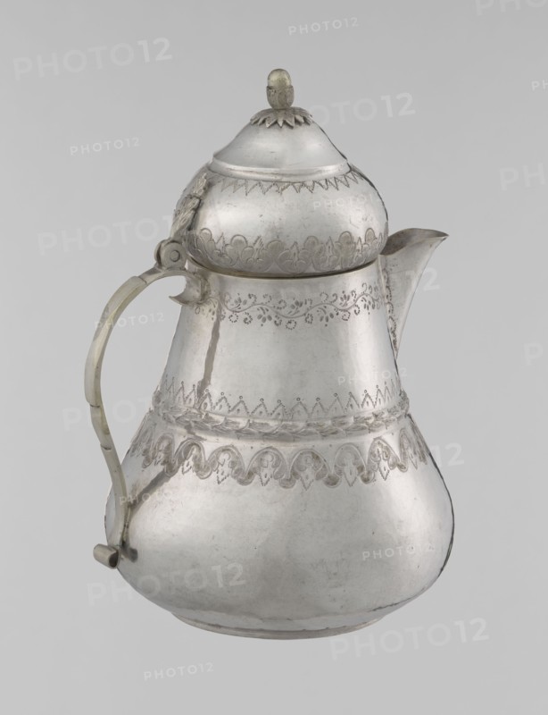 Teapot, Islamic art, Turkish, Ottoman dynasty 1299–1922; 19th century; Turkey. Materials/format: vessel teapot, height 17.0 cm, diameter 10.9 cm, weight 320 g. Decoration: geometric motifs, plant ornament, zigzag, lambrequin., A metal pitcher with a rounded body, a curved spout, and a hinged domed lid topped by a small finial, shown against a plain light gray background. The surface of the pitcher is primarily silvery-gray with areas of slightly darker patina and subtle scratches. Decorative engraved bands encircle the upper and middle sections, showing a repeating scallop and floral motif. The handle is a slightly different tone of gray and is attached to the body with visible rivets and a small curved terminal at the lower end. The lid has a serrated decorative rim where it meets the body and a petal-like detail beneath the finial. Overall the object presents a smooth, reflective metallic texture with engraved ornamentation.