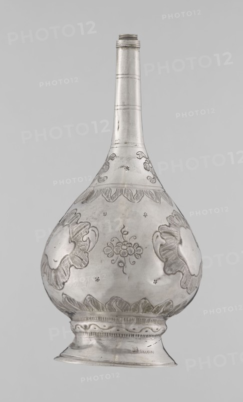 Bottle for spraying water soaked in perfumes, Islamic art; vessel with plant and floral ornament: multi-leafed undecorated cartouches alternating with small flowers; 19th/20th century; Turkey, / North Africa ; weight 113 g; height 17.5 cm; diameter 8.0 cm., A single metallic vessel with a long narrow neck and a rounded, bulbous body resting on a flared foot is shown against a plain light gray background. The vessel appears silver in color with darker engraved areas creating decorative patterns; the surface shows polished highlights and subtle variations of gray and reflective sheen. The bulbous body features engraved floral and foliate motifs including stylized flower clusters and petal-like shapes, with several scalloped bands encircling the widest part. The neck is smooth with a few incised horizontal bands and faint surface marks, and the foot has molded ridges and a repeating decorative engraved band around its upper edge. The overall appearance is metallic gray and silver with fin...