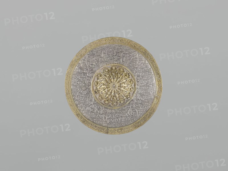 Mirror frame, scrap - purchase; Islamic art; mirror frame with plant motifs and geometric ornament including 6-pointed star Solomon's Seal; stylized plant patterns in a geometric arrangement; 19th century; Turkey, / Iran ; weight 685 g; diameter 25.5 cm; height 1.2 cm., A circular decorative object centered on a plain background, featuring a metallic appearance with a gold outer rim and an ornate gold patterned central medallion, surrounded by a silver-toned area embossed with intricate floral and vine motifs; the colors visible include gold, silver, and shades of gray, with the background appearing light gray.