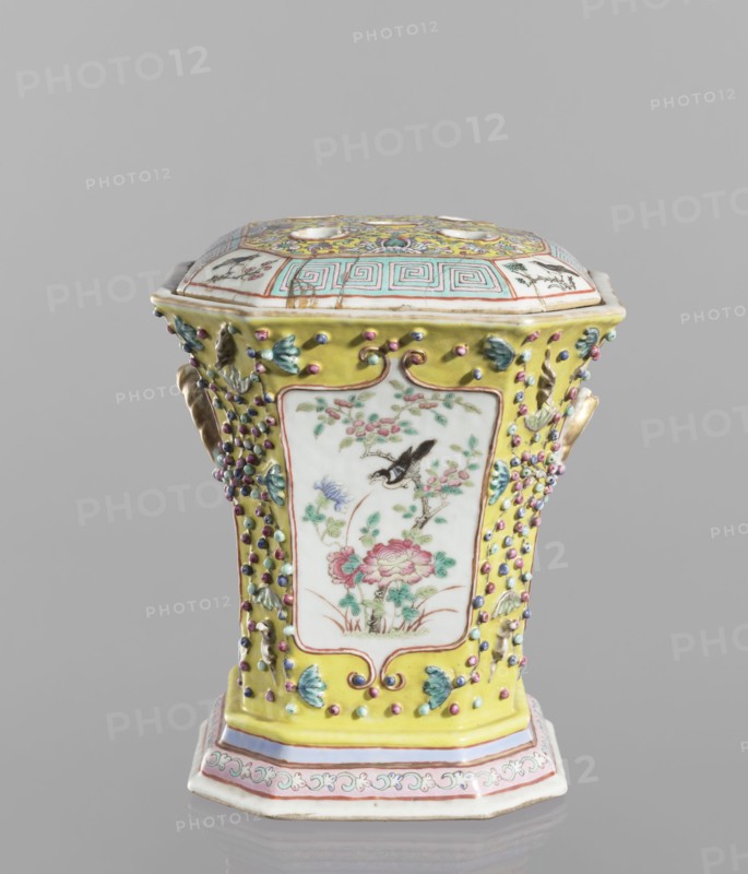 Vase with a lid, ceramics, colored porcelain, openwork flat perforated lid; decorated with flowers, birds, meander ornament, plant ornaments and lotus tendril motif; 19th century, China; vessel; height 27.0 cm, width 15.0 cm., A decorative hexagonal porcelain container with a fitted lid, predominantly yellow with accents of white, pink, green, blue, purple, and gold; the sides feature framed white panels painted with floral and bird motifs in green, pink, red, and black, surrounded by raised bead-like embellishments in purple, blue, and pink and small green leaf appliqués; the lid has geometric and floral designs in turquoise, yellow, pink, green, and gold on a white background; the base rim shows bands of pink, white, and gold with a scrolling decorative border.