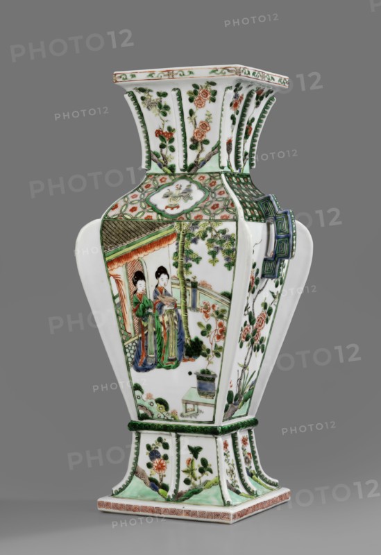 Hu-type vase, ceramics, green family, Kangxi style, hu vessel, vases, Chinese culture, Chinese art, Qing style, Qing 1644–1911, Kangxi 1662–1722, 1662–1722, China, vessel, height 39 cm, A tall, hexagonal porcelain vase with a flared neck and a square base stands against a neutral gray background; its surface is predominantly white with painted decorations in green, red, orange, blue, and black. The central panel shows two women in traditional dress rendered in green, blue, red, and orange standing beside architectural and garden elements painted in green and muted orange, with surrounding floral and bamboo motifs. Other panels feature stylized floral branches and blossoms in green, orange, and red, and a geometric handle-like decoration on one side in blue and green. The neck and base are decorated with vertical green ribbing and floral sprays in green and orange, and there is a patterned border along the top and bottom edges in green and orange tones. Overall the vase displays a mix o...
