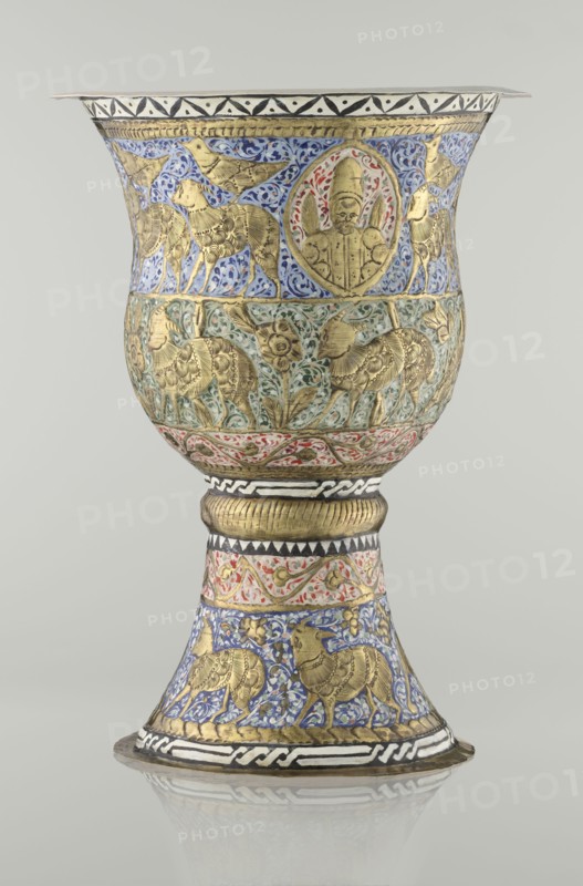 Cup, Persian, Qajar dynasty 1785–1925, 19th century, Iran. Vessel cup, height 25.5 cm, diameter 18.4 cm. Decoration: cartouches with a bust of a man, animals lions, birds, figures, flowers, geometric and small plant ornament; figurative motifs., A decorated goblet-shaped vessel with a flared rim and a flared foot standing on a reflective surface, featuring ornate embossed and painted ornamentation in gold, blue, green, red, white, black, and cream; the upper bowl area shows a band of blue background with gold animal figures and a central circular medallion containing a gold humanlike figure surrounded by red and green accents, while a lower band on the bowl has a greenish background with gold animals and floral motifs; the stem and foot display alternating decorative bands including a ribbed gold collar, a cream band with red scrolling foliage, and a blue band with gold animal figures, all separated by black-and-white geometric borders, with finely textured gold detailing throughout an...