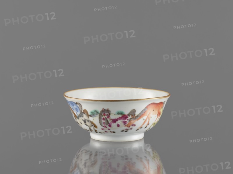 Bowl, ceramics, colored porcelain, Qing style, Chinese art, landscape motifs, Chinese culture, horses, bowl on a ring-shaped foot, decorated on the outer wall, 19th century, China, vessel, height 5 cm, diameter 11.8 cm, A small white porcelain bowl with a thin gold rim sits on a reflective gray surface against a gray background; the exterior of the bowl is painted with a group of colorful stylized animals and plants in shades of orange, pink, blue, green, black, and brown, and the bowl's interior is plain white.