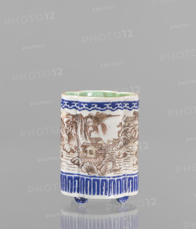 Bowl for tablecloths, ceramics, colored porcelain, fishermen, Chinese art, Qing style, landscape motifs, Chinese culture, incense, geometric ornaments, lambrequin pattern, containers, revindication provenance, Qing 1644–1911, Qianlong 1736–1795, Qianlong style, backdated signatures. Bowl on four small feet. Continuous landscape decoration, bordered at the top and bottom with geometric and lambrequin ornament. 19th century, China, bowl, height 8.2 cm, diameter 6 cm., A cylindrical ceramic cup standing on small rounded feet, predominantly white with hand-painted decoration; the upper interior shows a pale green glaze, the exterior features a deep blue decorative band near the rim and a matching deep blue patterned band near the base, with a brown linear landscape scene wrapping around the middle depicting houses, bridges, rocky formations, and trees rendered in fine brown lines; the small feet are glazed deep blue and the background behind the cup is a uniform light gray.