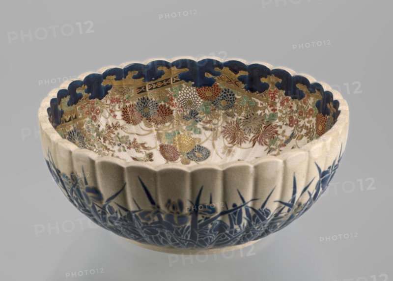 Bowl, Toyota Masanobu maker, signature on bottom in gold. Deep satsuma bowl on a low ring-shaped base, knobbed body with serrated rim resembling a chrysanthemum. Outer wall: clumps of blooming irises growing from water, flowers and leaves painted in two-tone blue enamel; stylized waves and ripples outlined in gold. Inner surface: large gold chrysanthemum rosette imperial coat of arms in the mirror with the Tokugawa family crest in the center; side wall filled with dense, colorful chrysanthemum flowers and butterflies painted in white, red, blue, gold, and green using overglaze enamels and gold. Top edge finished with a uniform cobalt blue valance ornament. Inscription reads: Satsuma yaki, Satsuma kuni, Ijun'in, Toyota Masanobu. 19th century Meiji period, Japan, Kagoshima. Ceramic vessel; height 12.0 cm, diameter 28.0 cm., A scalloped ceramic bowl shown against a neutral background with a pale exterior and deep blue painted floral motifs along the lower outer surface, a scalloped rim pa...