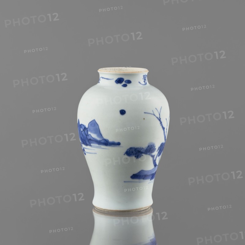 Meiping-type vase, ceramics, Meiping vessel type, blue-and-white porcelain, Qing style 1644–1911, landscape motifs including rocks, trees, and a pagoda; neck decorated with small plant motifs, Chinese, 1662–1722, vessel, height 17.7 cm, diameter 11.8 cm, A white ceramic vase with a rounded body, a slightly narrowed neck, and a small flared rim sits against a grey background; the vase features blue painted landscape motifs including stylized mountains, a tree with bare branches, and abstract cloudlike or foliage shapes, with decorative blue dots and brushstrokes near the neck and scattered on the body; the rim and base show a faint beige tint, and the overall visible colors are white, blue, beige, and grey.