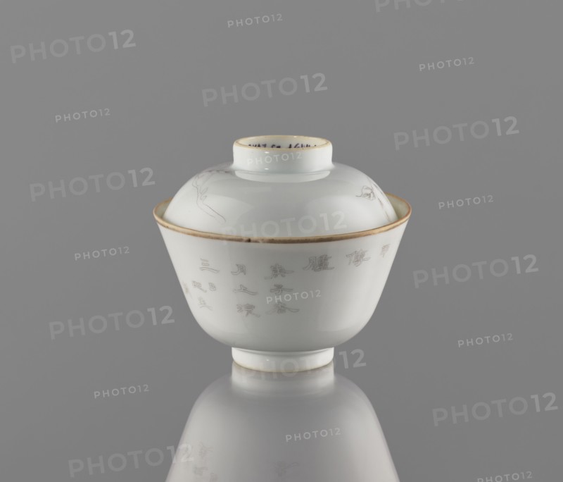Bowl with a lid, ceramics, colored porcelain; decorated with ducks among reeds drawn in delicate black line and an inscription; lid topped with a branch bearing peach fruit. Qing dynasty, Tongzhi period 1862–1874. Bowl on a ring foot with a lid-stand. China; height 9 cm, diameter 10.3 cm., A white glazed porcelain covered bowl with a round foot and a domed lid sits centered against a neutral gray background; the bowl and lid have a thin gold rim and faint engraved linear designs visible on the lid and body, and the smooth glossy surface produces soft reflections on the gray surface beneath; visible colors include white, gray, and gold.
