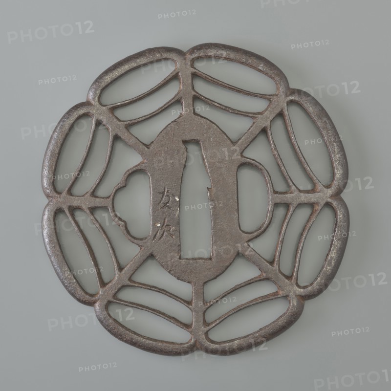 Crossguard tsuba, Tomotsugu, Japanese art, Japanese culture, Edo 1603–1868, swords, weapons, melee weapons, katana, sword crossguards, openwork, Tsuba sukashi in the shape of a seven-petaled mokkô rosette, with openwork petals divided by arched lines forming a spiderweb pattern, with integrally woven ryôhitsu ana holes and an oval seppa dai. Signed. 19th century, Edo period 1603–1868, Japan, tsuba, height 8.0 cm, width 7.8 cm, depth 0.6 cm, A round metal object with an openwork floral or petal-like pattern, showing a central elongated oval opening flanked by a rectangular cutout and a scalloped shape, all surrounded by a ring of curved, connected petal shapes; the metal surface appears dark brown to rusty with areas of lighter brown and gray patina, and the background is a smooth pale gray.