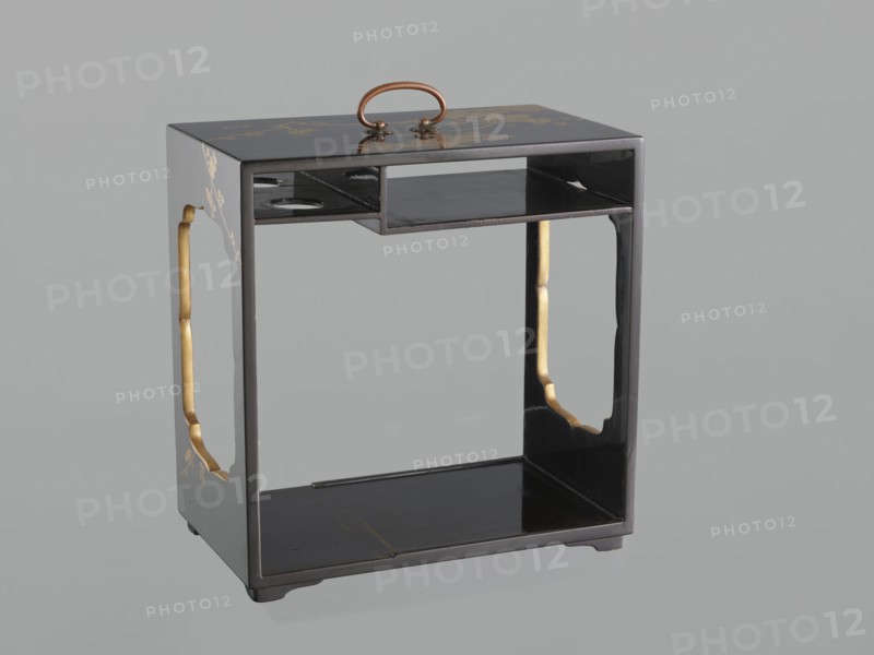 Portable picnic set sagejûbako, Rectangular cabinet without side walls on a stand with two stacked food containers set incomplete; originally four; beside them on the stand are two tin sake bottles. Top tabletop has a handle, one small drawer, and a shelf for trays missing. Entire exterior covered with black roiro-nuri lacquer; interiors of food containers with vermilion lacquer. Surface ornament executed in hiramaki-e and nashiji techniques, depicting blooming wisteria, camellias, and rosettes/coins; also motifs of leaves, plum trees, and wolfberries; includes mon. Such portable eating sets were called in Japan kôchû, sagejû, hanami bentô and were popular from the Momoyama period mid-16th–early 17th c. and in the 18th–19th centuries. 19th century Edo–Meiji periods, Japan. Height 31.3 cm; width 30.5 cm; depth 17.8 cm; weight 2.29 kg., A small rectangular wooden stand with a glossy black finish and a rounded brass handle on top; the stand has an open central compartment with a raised sh...