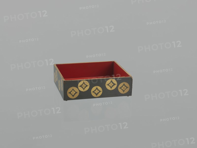 Portable picnic set sagejûbako, Rectangular cabinet without side walls. On a stand there are two food containers stacked on top of each other set incomplete; originally four; next to the containers on the stand are two tin sake bottles. The top tabletop, equipped with a handle, has one small drawer and a shelf for trays missing. Entire surface covered with black roiro-nuri lacquer; interiors of the food containers covered with vermilion lacquer. Ornament executed in hiramaki-e and nashiji techniques depicting blooming wisteria, camellias, rosettes coins, mon, leaves, plum trees, and wolfberries. Such portable eating sets were called variously in Japan kocho, sageju, hanami bento and were popular from the Momoyama period mid-16th–early 17th century, and in the 18th and 19th centuries. 19th century Edo–Meiji periods, Japan. Dimensions: height 31.3 cm, width 30.5 cm, depth 17.8 cm; weight 2.29 kg., A shallow rectangular box with an open top sits on a reflective surface; the interior is re...