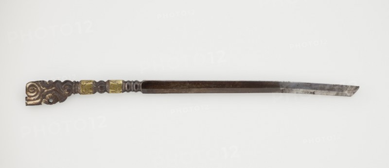 Dagger, craft, Tibetan, militaria, daggers weapons, 19th century, Tibet place of origin?, weapon, height 25.8 cm, A long, slender metal object with a straight, tapered blade on one end and an ornate handle on the other; the blade is silvery gray with darker gray patches and some surface discoloration, transitioning into a darker brown shaft; the handle is carved with flowing, scroll-like shapes in dark brown with areas of lighter tan, and it includes a couple of decorative metallic bands in a muted gold color; the overall background is plain off-white.