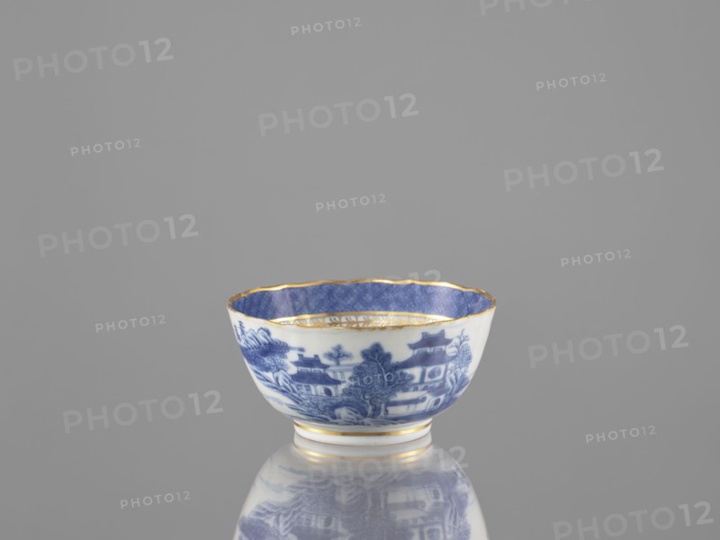 Teapot, ceramics, blue-and-white porcelain, Qing dynasty 19th century, 1644–1912, Chinese, landscape motifs; part of a 22-piece tea and coffee service teapot, 6 cups, 6 goblets, 6 saucers, a bowl, a cover, and a plate; vessel; height 7 cm, diameter 14.3 cm., A small porcelain bowl sits on a reflective surface, showing a blue and white exterior decorated with a scenic pattern and a blue interior with a subtle geometric design; the rim and a few bands near the base are accented in gold, and the background is a uniform gray.
