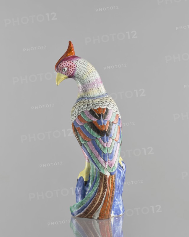 Rooster figurine, Chinese, Qing dynasty 1644–1911, 19th century; colored porcelain ceramics; sculpture depicting a rooster with rocks; animals/birds iconography; height 28.5 cm, width 14.5 cm., A colorful ceramic bird figurine perched on a textured ceramic base, shown from the back and slightly turned to the side; the bird has a red crest, a yellow beak, and a head with pale tones and dotted markings, while its body is covered in layered, scalloped feathers painted in a palette of green, blue, pink, purple, orange, brown, black, and white, with the base displaying blue and brown tones and a glossy finish, all set against a plain gray background.