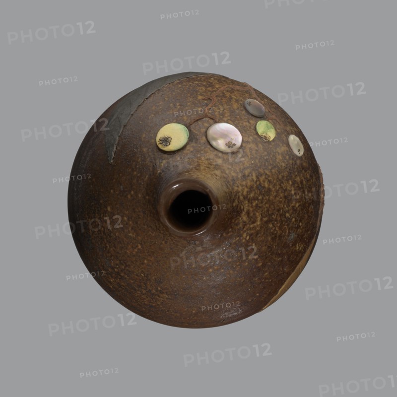 Sake bottle tokkuri, gift; Japanese art; Edo 1603–1868–Meiji 1868–1912; bottle for sake; A bottle with a spherical belly and a narrow cylindrical neck; covered with brown glaze which in the upper part of the belly and on the neck turns light coffee-coloured and becomes spotted. Decorated on the belly with a branch of biwa Japanese medlar, fruits made with green-yellow glaze and inlaid with mother-of-pearl, leaves made using the technique of sprinkling on black lacquer. 19th century, Japan, Bizen; vessel; height 18 cm, diameter 11.8 cm., A round, bulbous ceramic vessel viewed from above with a central round opening, showing a textured surface in shades of brown and rust with speckled darker brown areas; a few small round decorative discs in pale green, iridescent pearly white, and muted yellow are arranged near the top edge, and there is a dark, rough patch of material or repair on one side; the background is a flat gray.